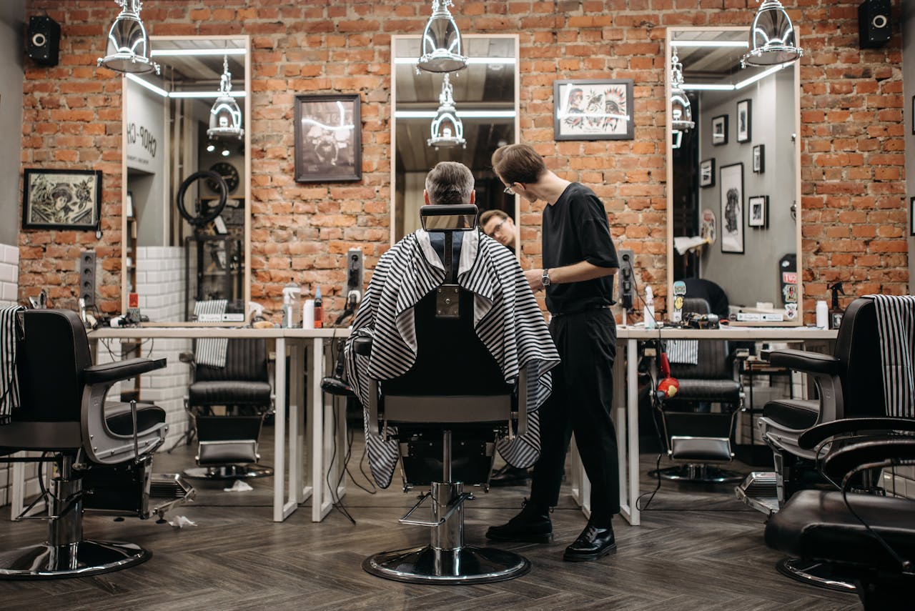about-us-02 A skilled barber attending to a client in a stylish barbershop with exposed brick walls.